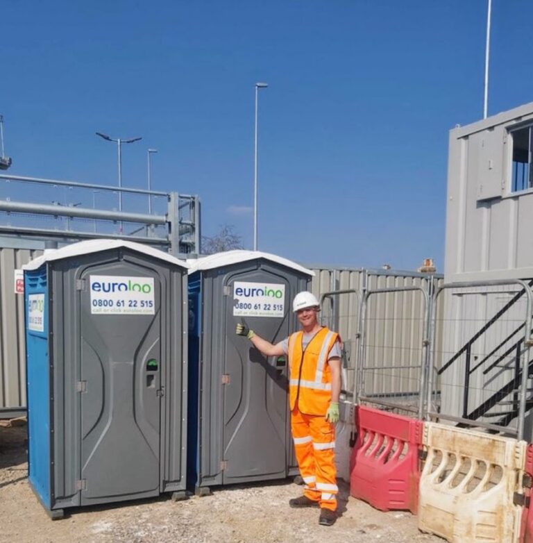 Construction Worker Giving A Thumbs Up Next To Two Euroloo Portable Site Toilets On An Active Building Project.