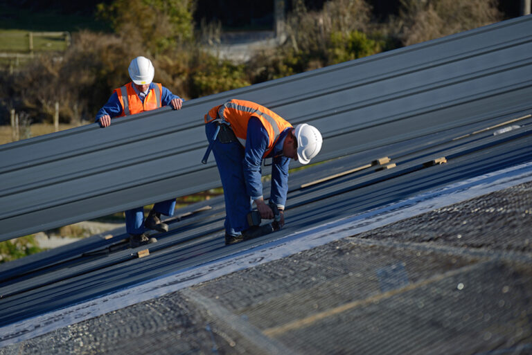 Two Industrial Roofing Contractors Working On A Commercial Roof During Envelope Works.